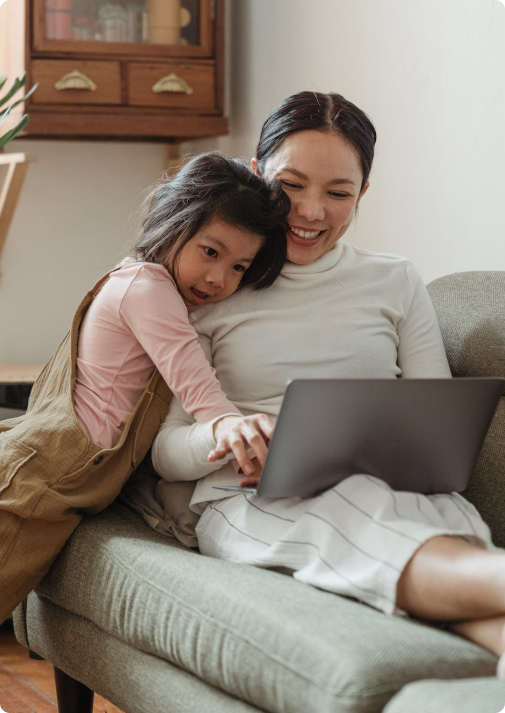 Young girl hugging mother working on laptop on couch
