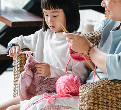 Grandma teaching young girl how to knit with pink yarn